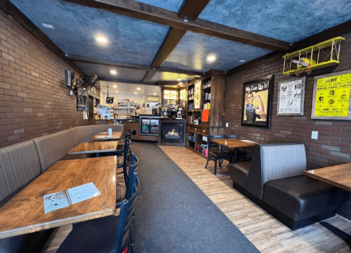 Cozy café interior with wooden tables, brick walls, and a counter in the background. Warm lighting creates a welcoming atmosphere.